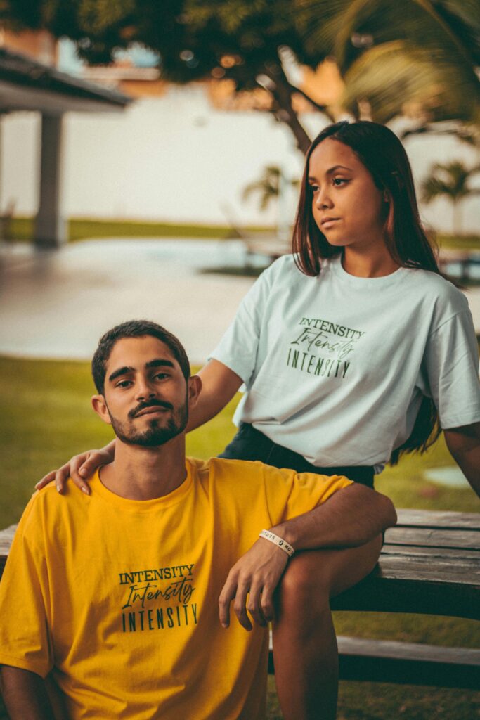A young couple sitting on a wooden table outdoors, expressing casual fashion and relaxation.